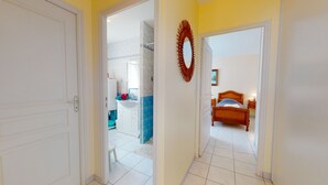 A hallway leading to a bathroom with a shower and a bedroom with a bed.