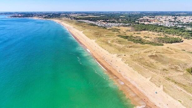 An aerial view of a coastal area with a sandy beach and clear turquoise waters.