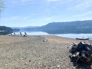 Une plage de galets avec des chaises longues et une jetée qui s’avance dans des eaux calmes, le tout entouré de collines.