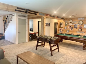 Une pièce équipée d’un baby-foot, d’une table de billard et d’un banc en bois. On y trouve un escalier avec une rampe et une porte portant l’inscription « WHITBY RD. ».