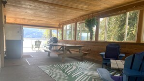 A covered outdoor seating area with a picnic table, chairs, and a grill. - Sunnyside Lakehouse - Semi-waterfront Shuswap Accommodation (Celista)