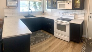 A kitchen with a white countertop, dark cabinets, a built-in microwave, and a stove. - Sunnyside Lakehouse - Semi-waterfront Shuswap Accommodation (Celista)