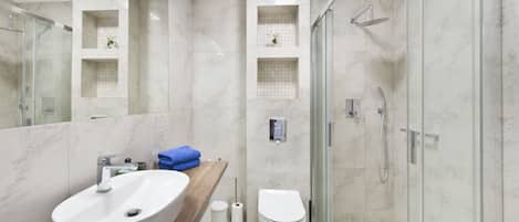 A modern bathroom with a large white sink, a toilet, and a glass-enclosed shower.
