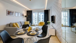 A modern living room with a sofa, dining table, chairs, and a TV. - Angielska Grobla by Q4 Apartments  (Gdansk)