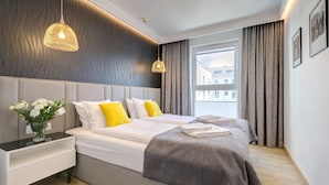 A modern hotel room with a large bed, bedside tables, a vase of flowers, and a view of buildings through the window. - Angielska Grobla by Q4 Apartments  (Gdansk)
