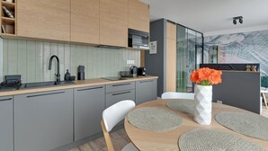 A modern kitchen with grey cabinets, a wooden countertop, and a dining area with a round table and chairs. - Angielska Grobla by Q4 Apartments  (Gdansk)