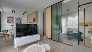 A modern living room with a flat-screen TV, a dining area, and a glass sliding door leading to a balcony. - Angielska Grobla by Q4 Apartments  (Gdansk)