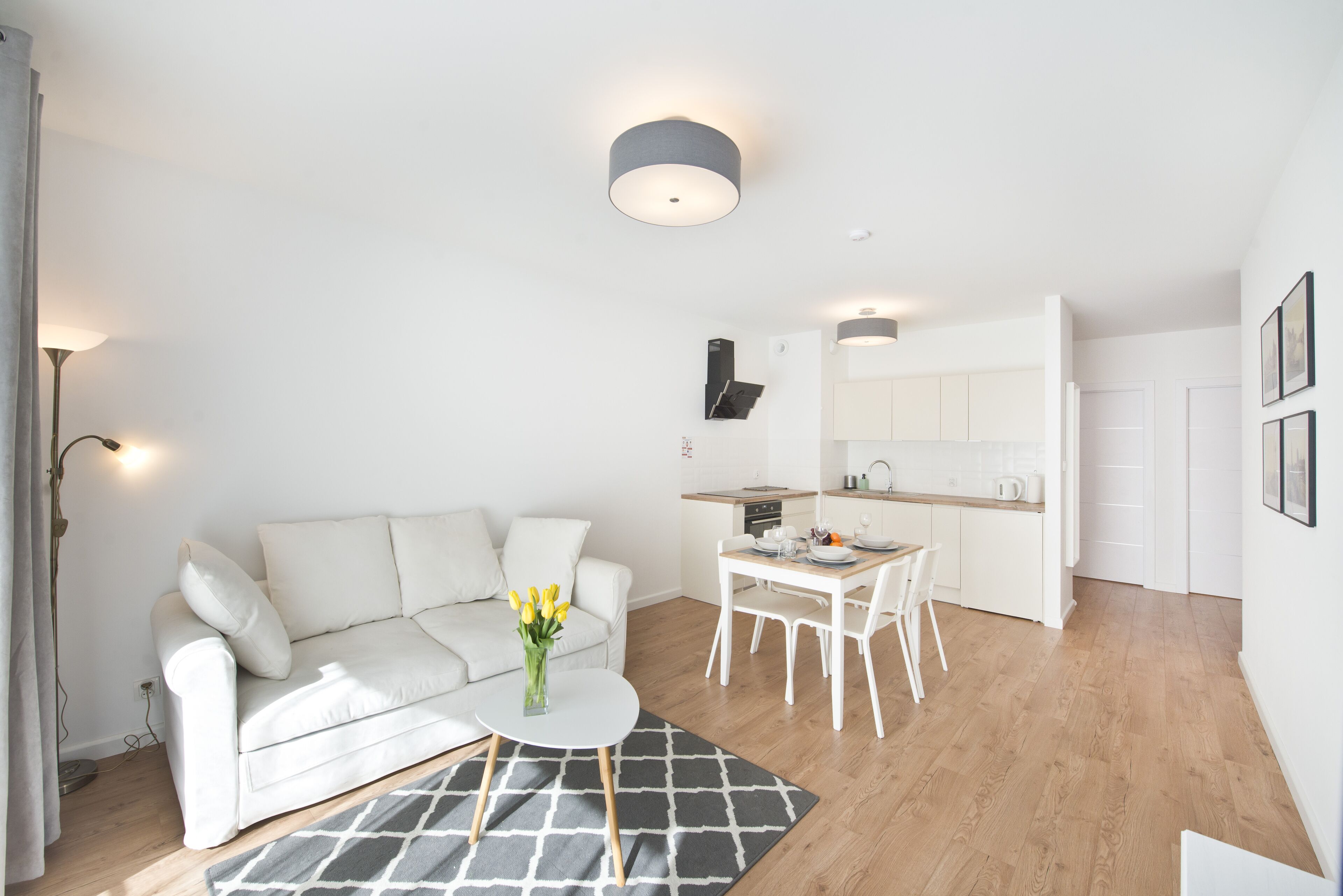 A modern, compact living space with a white sofa, a dining table, and a kitchen area.
