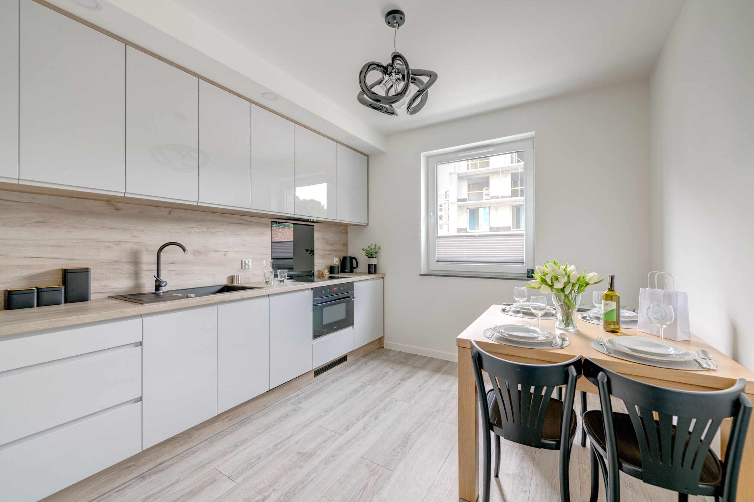 Una cocina moderna con armarios blancos, encimera de madera y horno empotrado. Cuenta con un comedor con mesa de madera y sillas negras.