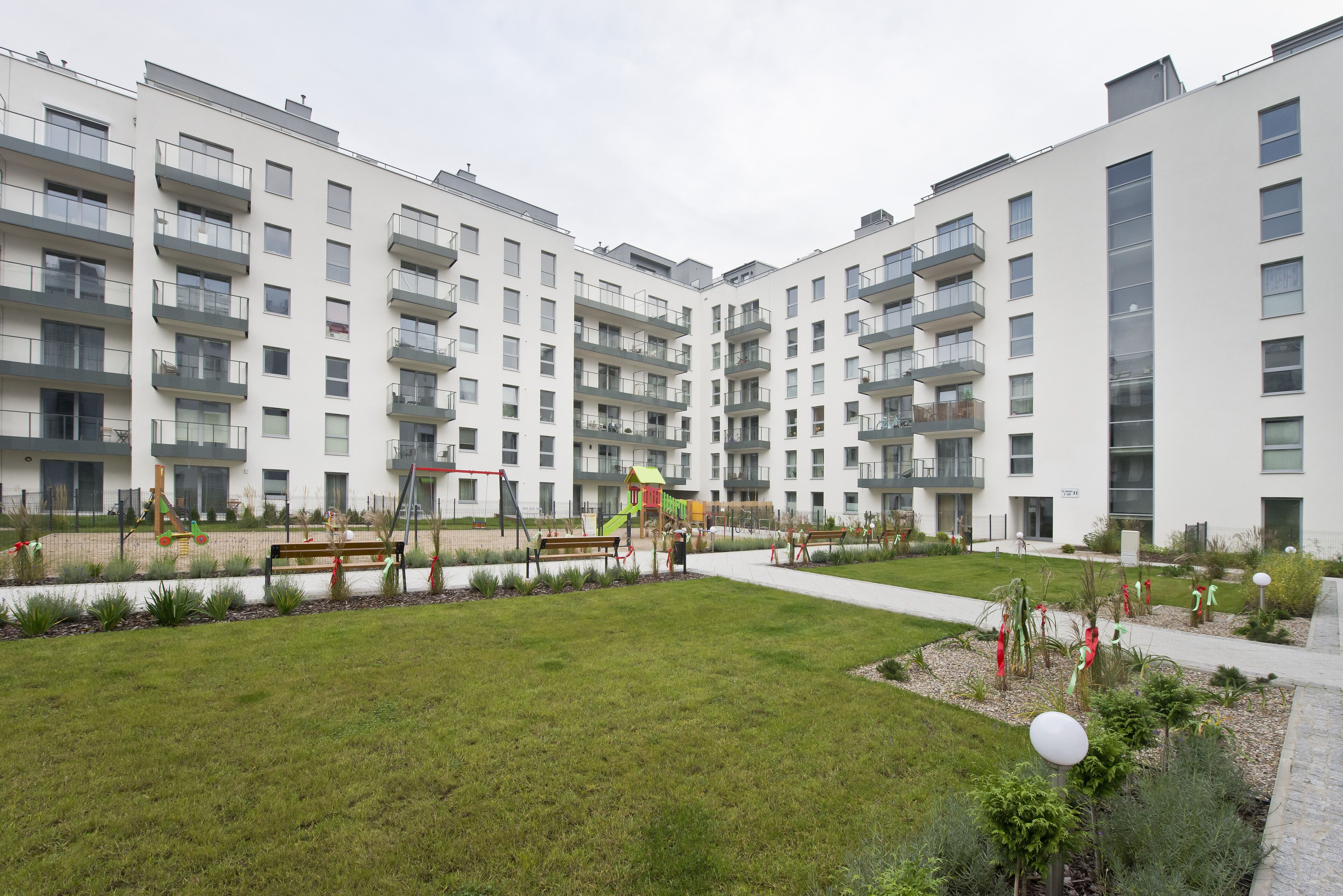 Un moderno complejo de apartamentos con varios balcones, un parque infantil y un jardín bien cuidado.