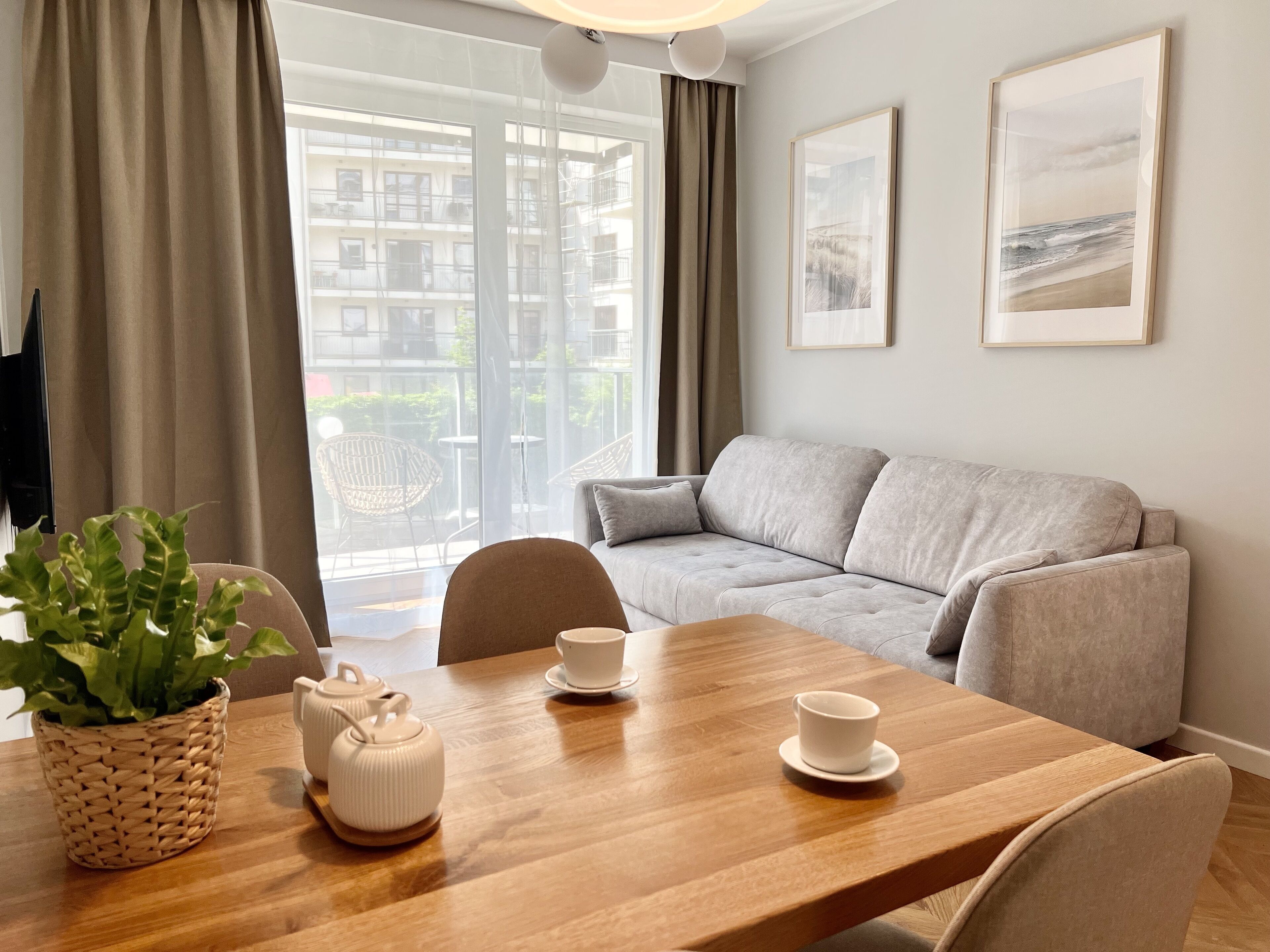 Ein modernes Wohnzimmer mit einer Couch, einem Esstisch mit Stühlen, einem Topfpflanzen und zwei gerahmten Bildern an der Wand.
