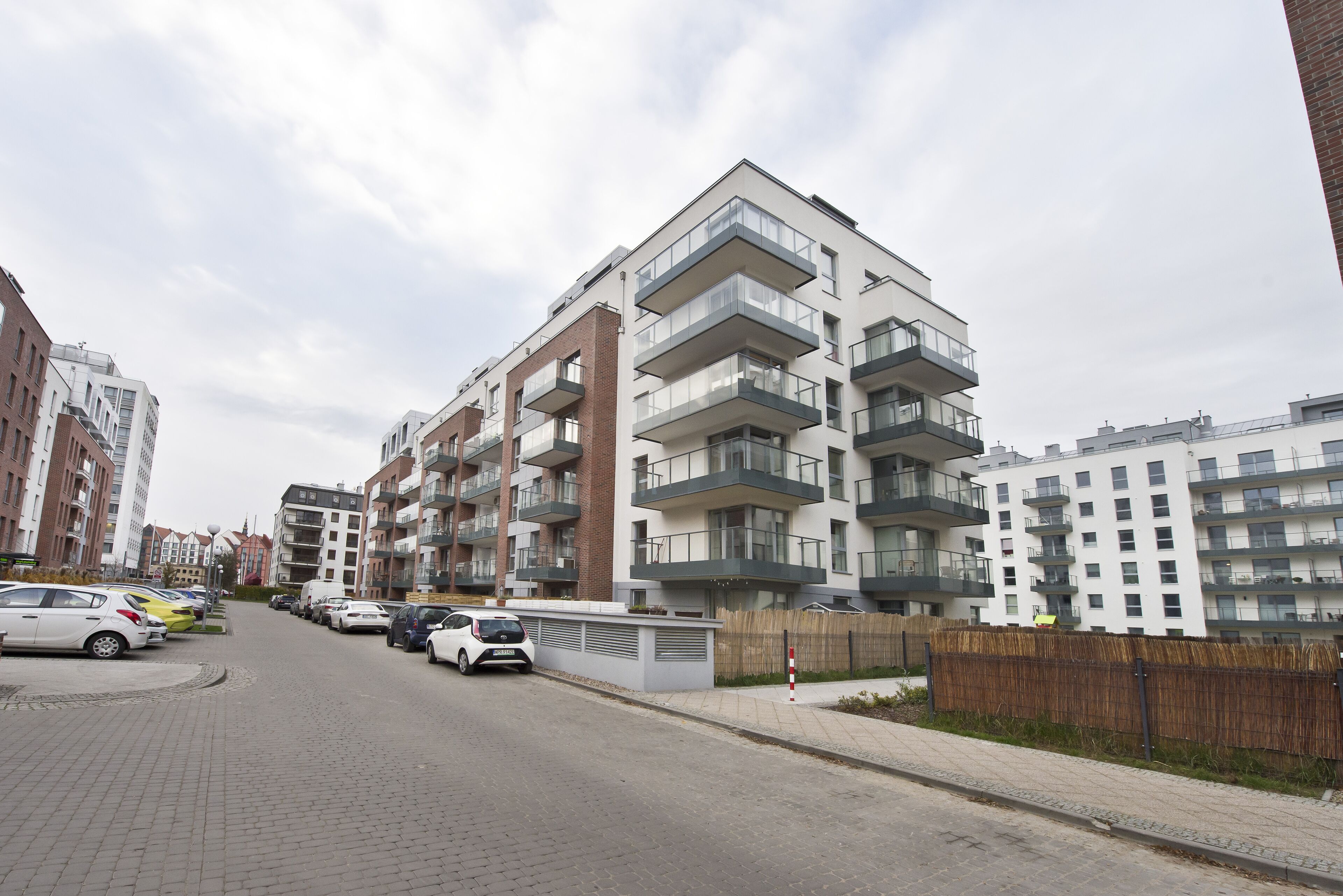 A modern apartment building with multiple balconies, a paved street, and parked cars.