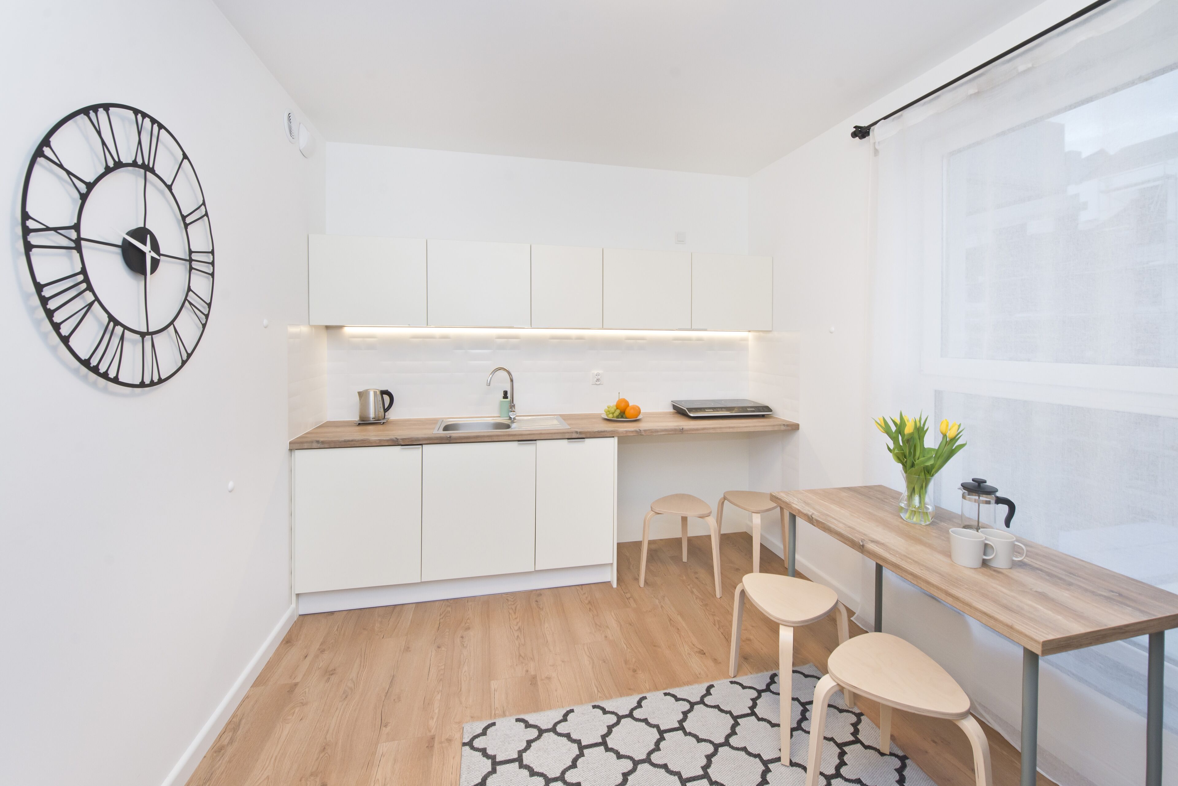 Una cocina moderna con armarios blancos, encimera de madera, cafetera y un reloj en la pared.