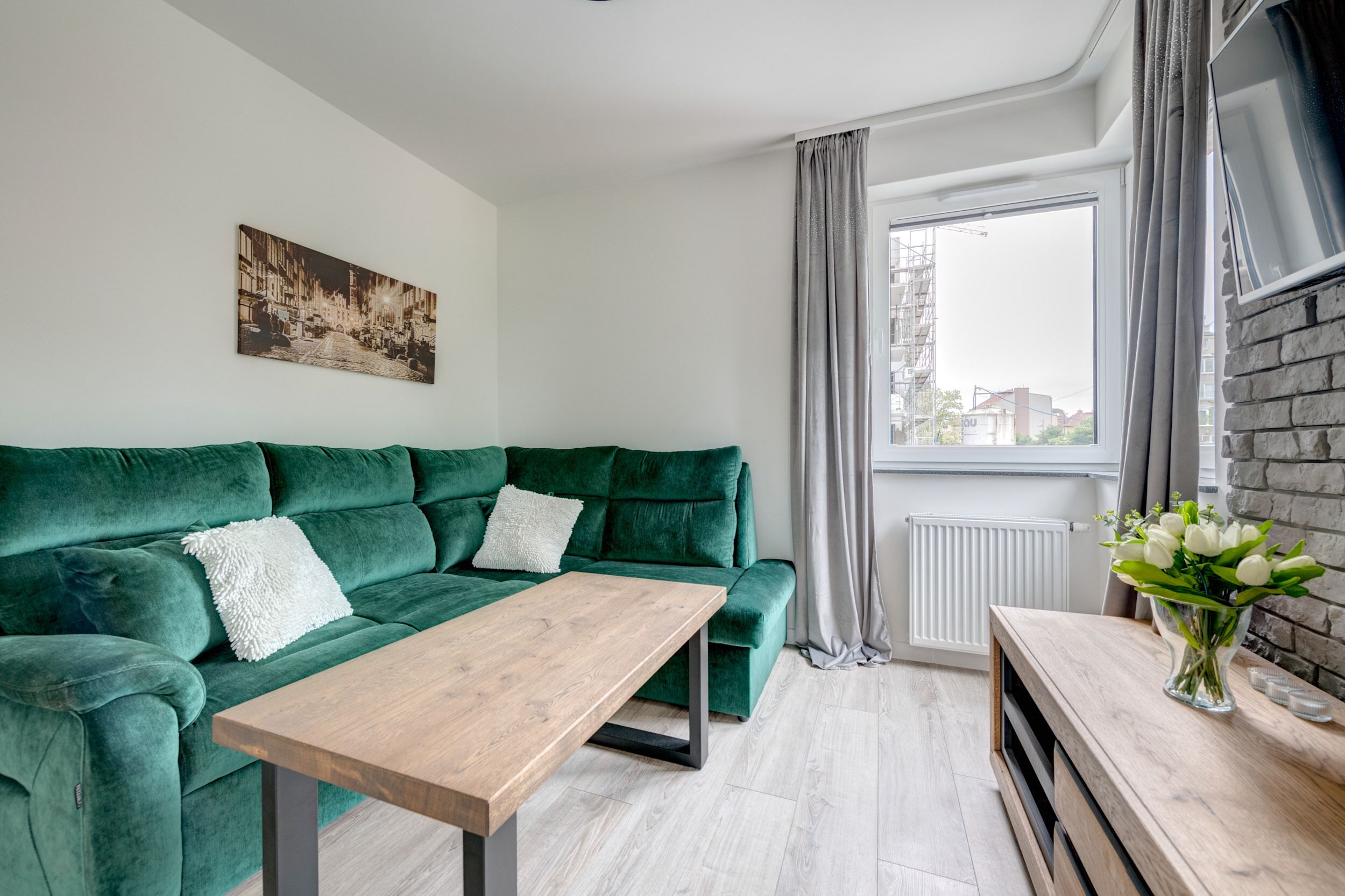 A modern living room with a green sofa, a wooden coffee table, and a cityscape painting on the wall.