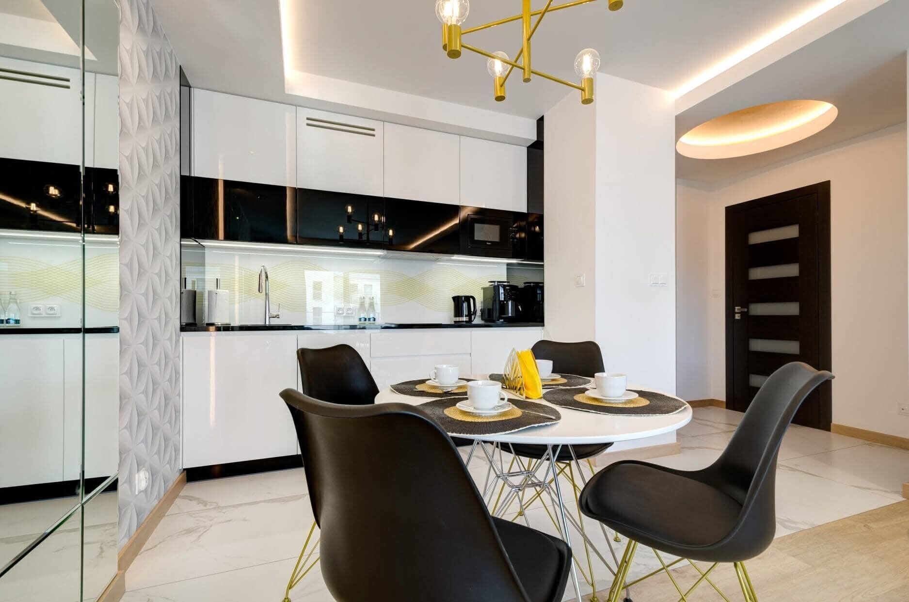 Une cuisine moderne avec des meubles blancs, un plan de travail noir et un coin repas comprenant une table ronde et des chaises noires.