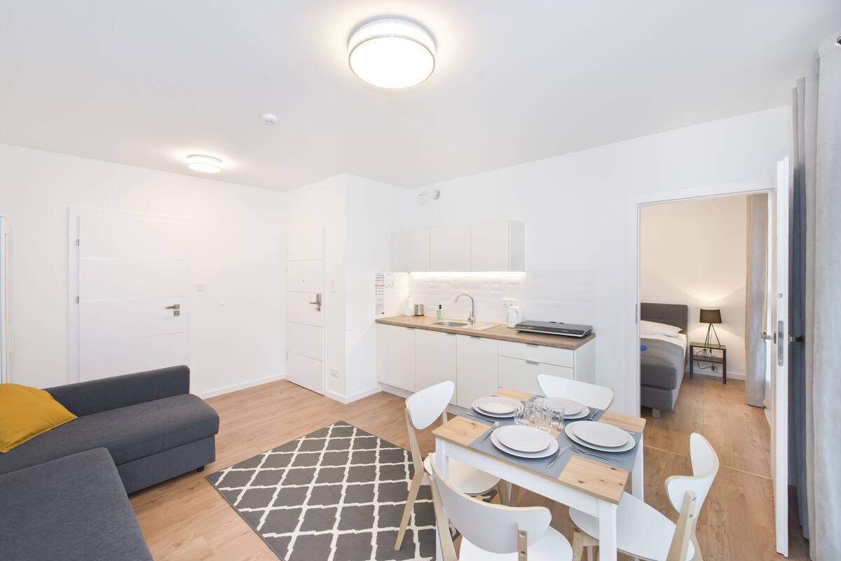 A modern apartment with a dining area, kitchenette, and a living room with a sofa and a patterned rug.