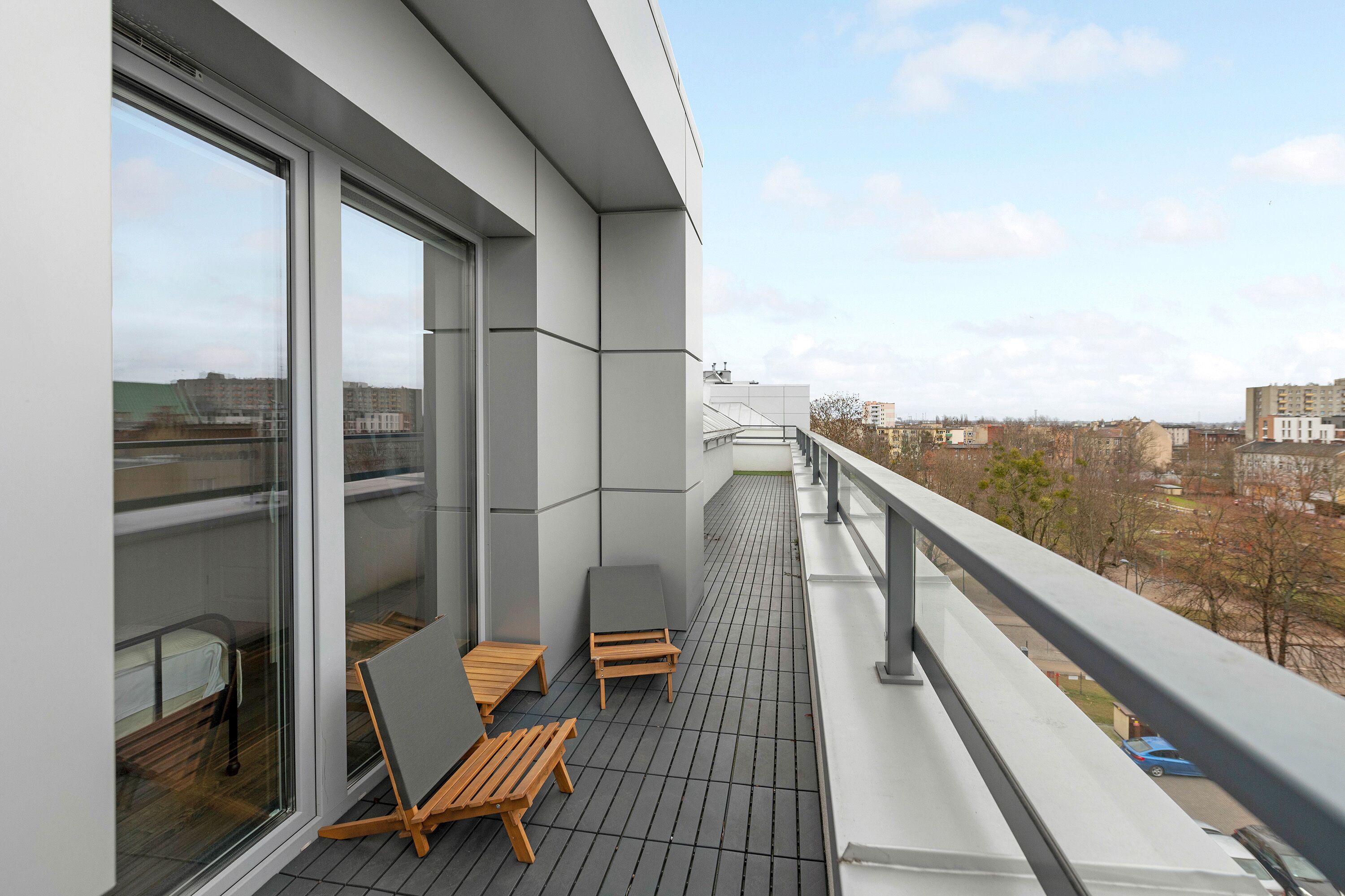 A balcony with a view of the city, wooden chairs, and a table.