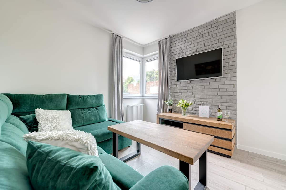 A modern living room with a green sofa, a wooden coffee table, and a TV mounted on a brick wall.