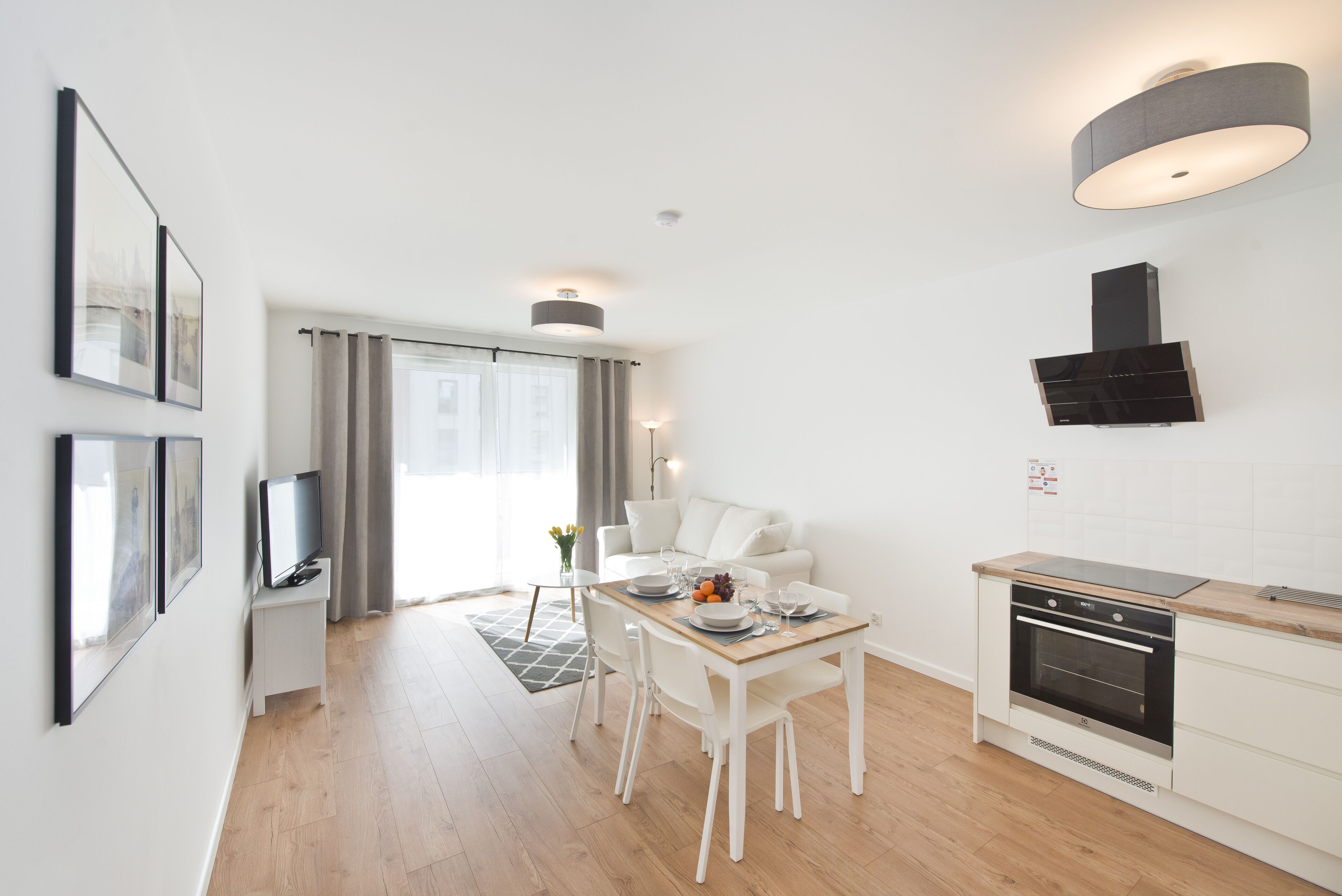A modern kitchen with a built-in oven, a dining area with a table and chairs, and a TV on a stand.