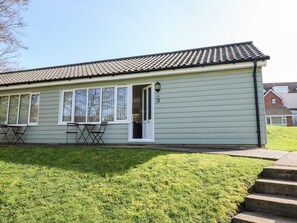 A single-story building with a tiled roof, a front door, and a small patio area with a table and chairs. - 14 The Dell (Norwich)