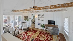 Un salón amplio con techo alto, una viga de madera grande, un tapete rojo estampado y un televisor sobre un mueble de madera.