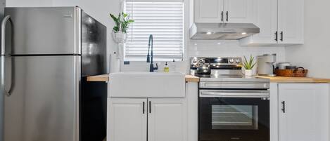 A modern kitchen with white cabinetry, stainless steel appliances, and a window with blinds.