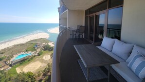 Een balkon met uitzicht op het strand en de oceaan. Er staat een tafel en een sofa met kussens.