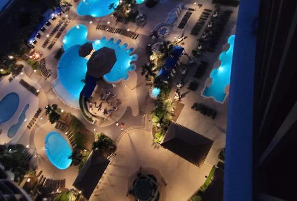 An aerial view of a resort with multiple swimming pools, lounge areas, and a central circular seating area.