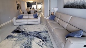 Een moderne woonkamer met een beige bank, een groot abstract vloerkleed en een plafondventilator.