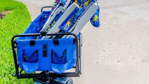Une chaise de plage à motifs colorés et recouverte d’une housse bleue, placée devant une maison avec un garage, et un vélo visible au fond.