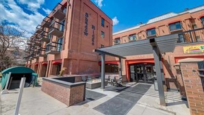 Un bâtiment à la façade en briques rouges et doté de balcons, un espace extérieur couvert avec des coins salon et des foyers, et une enseigne indiquant « Ski et snowboard ».