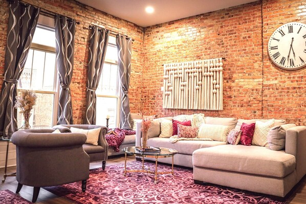 A living room with a brick wall, a large clock, two sofas, and a patterned rug.