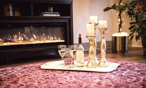 A fireplace with a fire, a tray with glasses and a bottle, and candles on a table.