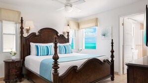 A bedroom with a wooden bed, a nightstand, a ceiling fan, and a view of the ocean through the window. - OCEANFRONT GRACE BAY top floor Coral Gardens (Providenciales)