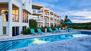 A modern hotel with a swimming pool, sun loungers, and a view of the surrounding landscape. - OCEANFRONT GRACE BAY top floor Coral Gardens (Providenciales)