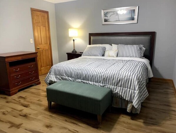 A bedroom with a bed, a nightstand, a dresser, and a door.