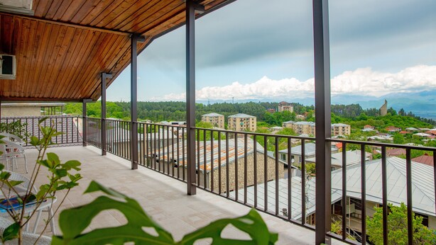 A balcony with a wooden ceiling and metal railings, overlooking a residential area with houses and trees.