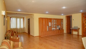 A spacious living room with a wooden floor, a sofa set, a wooden cabinet with glass doors, and a small table.
