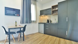 Una cucina moderna con pensili scuri, un tavolo da pranzo in legno con due sedie e un piccolo frigorifero.