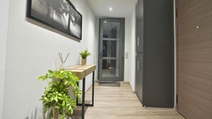 Un corridoio con pavimento in legno, una porta, un quadro appeso al muro e un piccolo tavolino con una pianta.