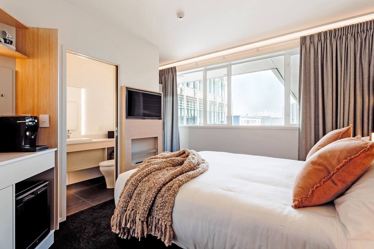 Een hotelkamer met een bed, een bureau, een koffieapparaat, een televisie en een raam met gordijnen.