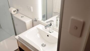 A modern bathroom with a white sink, chrome faucet, and a toilet with a paper towel holder.