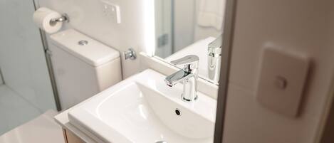 Un baño moderno con lavamanos blanco, grifo cromado y un inodoro con dispensador de toallas de papel.