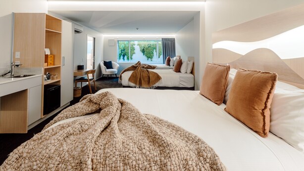 Een moderne hotelkamer met een groot bed, een bureau, een stoel en uitzicht op groen buiten het raam.