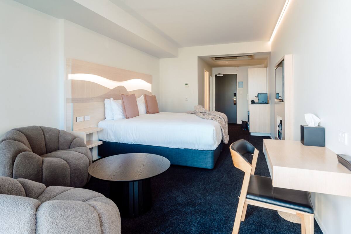 Een moderne hotelkamer met een groot bed, een bureau, een ronde salontafel en een bank.