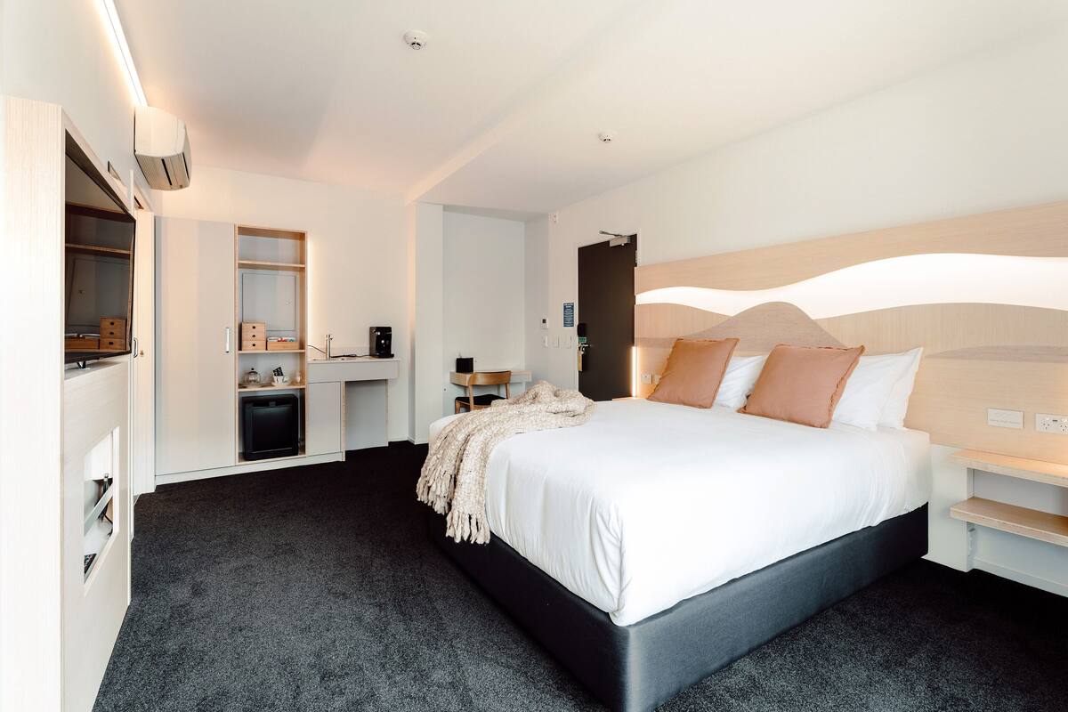 Een moderne hotelkamer met een groot bed, een inbouwkast en een kleine kitchenette.