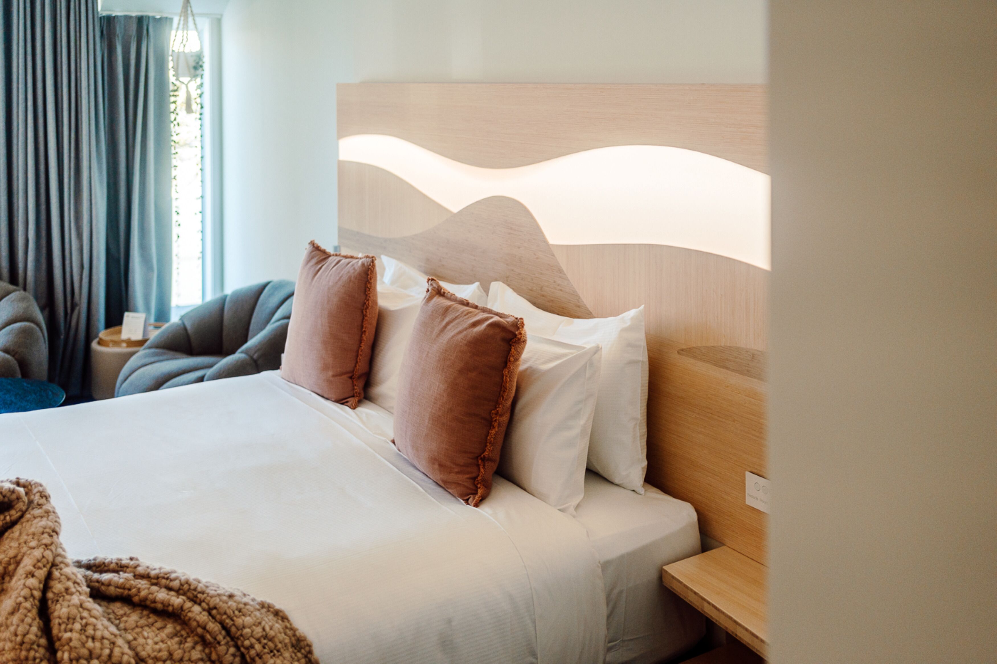 Una cama bien hecha con cabecera de madera, una mesita de noche y una silla.
