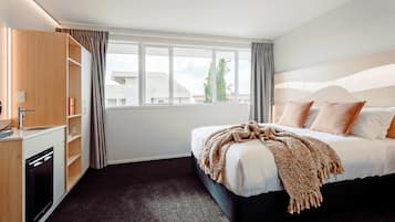 Habitación de hotel con cama, escritorio integrado y lavamanos, y ventana con cortinas.