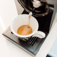Una cafetera sirviendo café en una taza blanca.