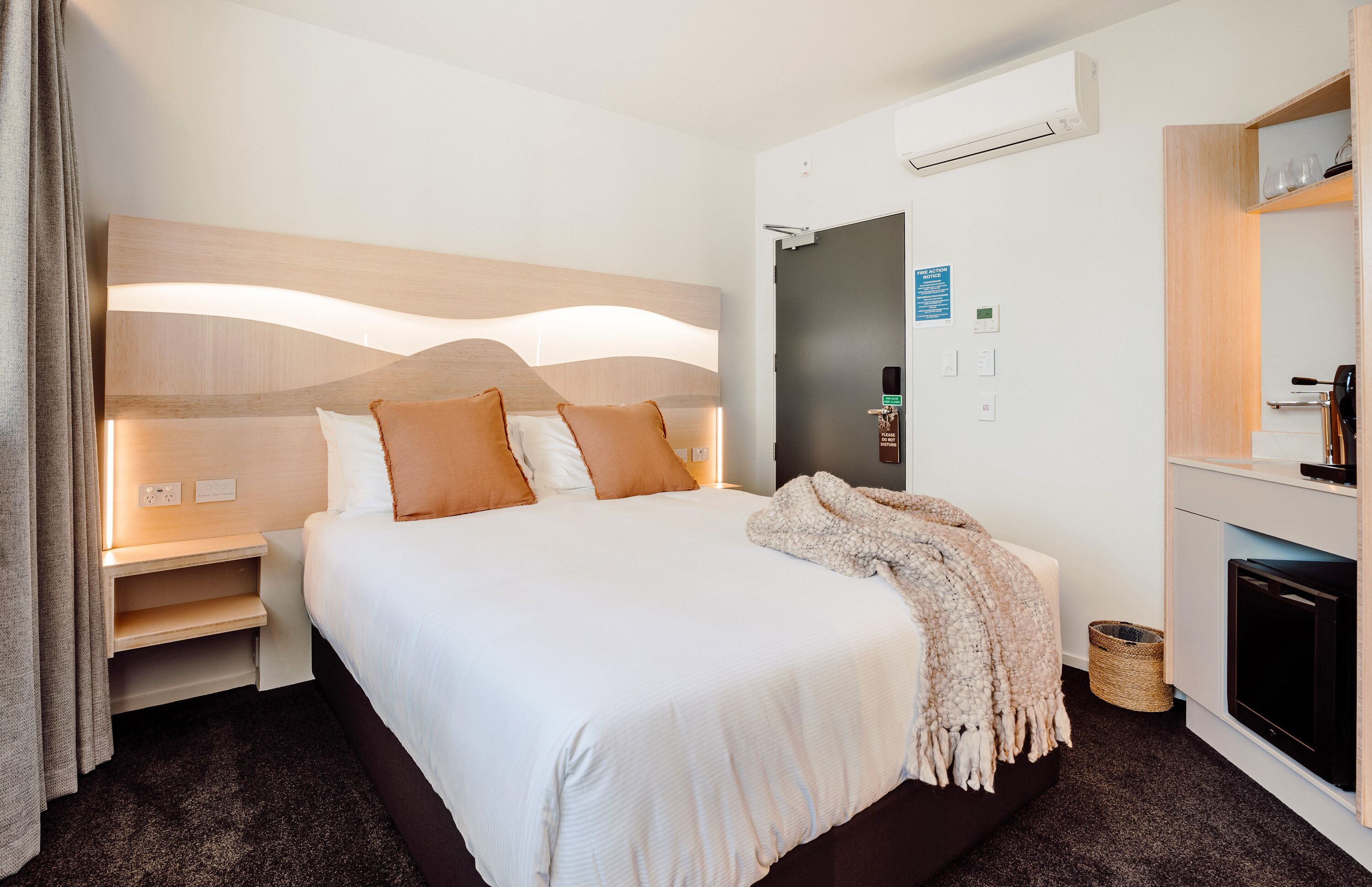 A hotel room with a large bed, bedside tables, a TV, and a mirror.